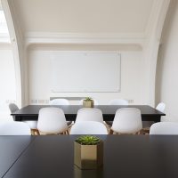 一位编辑在白板上画出台风路径弧线与影响半径示意，用橙红马克笔标注危险半圆，室内光线明亮